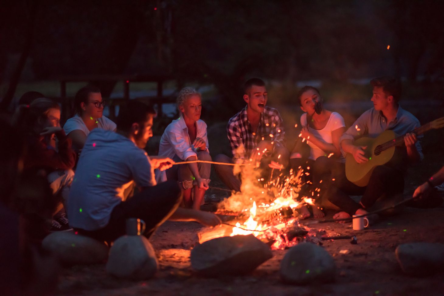 Image of people setting around a campfire roasting marshmallows. 